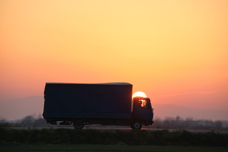 Cargo truck driving on highway hauling goods in evening. Delivery transportation and logistics concept.