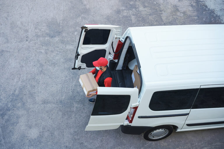 Top view of delivery man delivering package in front of cargo truck wearing safety mask - Focus on face